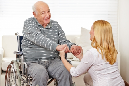 woman holding hands of old man in wheelchair in a nursing home