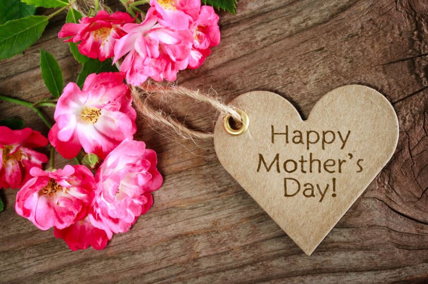 Mother's Day decoration next to flowers on wooden background