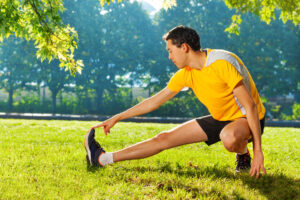 Flexible young man stretching legs outdoors practicing mobility movements