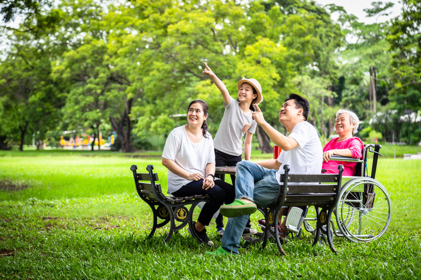 Happy Asian family; father,mother,daughter watching something interesting with senior grandmother in wheelchair in outdoor park.