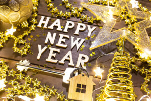 House key with keychain cottage on a festive background with sequins, stars, lights of garlands. Happy New Year-wooden letters, greetings, greeting card