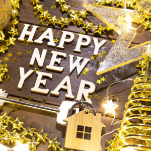 House key with keychain cottage on a festive background with sequins, stars, lights of garlands. Happy New Year-wooden letters, greetings, greeting card