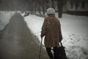 Woman walks in snow down street with cane