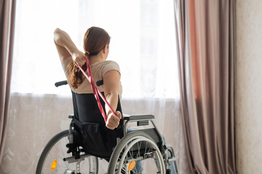 Caucasian woman in a wheelchair doing exercises with the help of fitness rubber bands.
