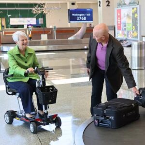 Senior couple getting their bags at baggage claim. Older woman in mobility scooter.
