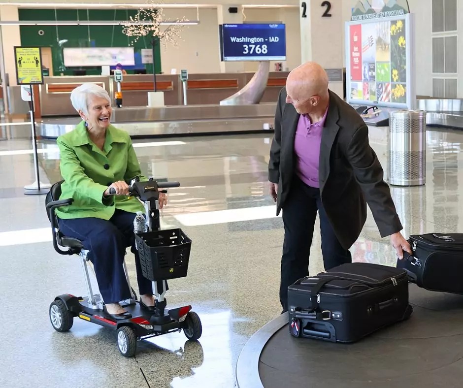 Senior couple getting their bags at baggage claim. Older woman in mobility scooter.